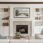 A framed TV beautifully mounted above a white brick fireplace, demonstrating how the warm walnut finish seamlessly blends a 75-inch TV into your elegant living room built-ins.