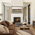 A beautiful 55-inch framed TV displaying a serene landscape over a modern fireplace, bringing a touch of warm walnut wood to a cozy, earth-toned living room.