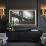A 50-inch framed TV displaying striking black and white photography in a modern, dark lounge, using the gold and white frame to add a beautiful pop of contrasting elegance.