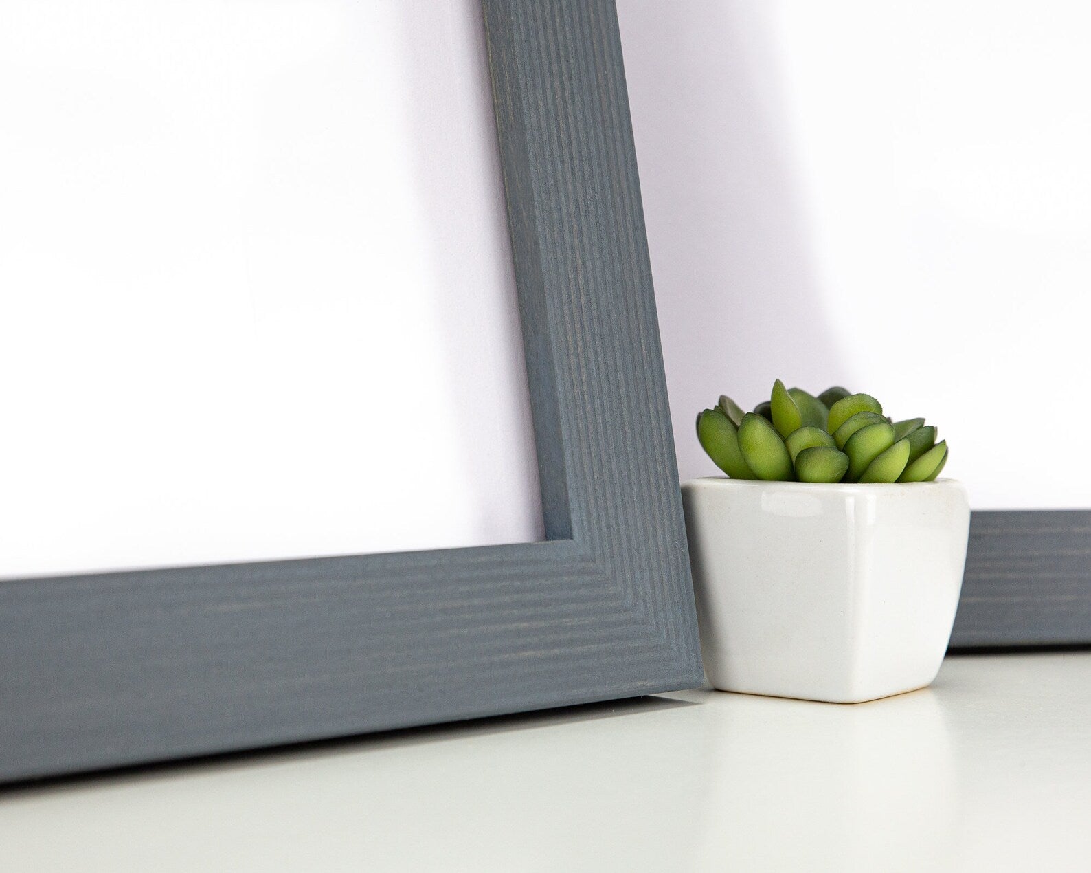 Gray picture frame on a white surface with a small potted plant in the corner. Grey Wooden Picture Frame, Handmade Custom Size Photo Frame, Stripy Design Poster Frame A1 A2 5x7 10x10 8x10 12x18 16x20 18x24 20x30 24x36