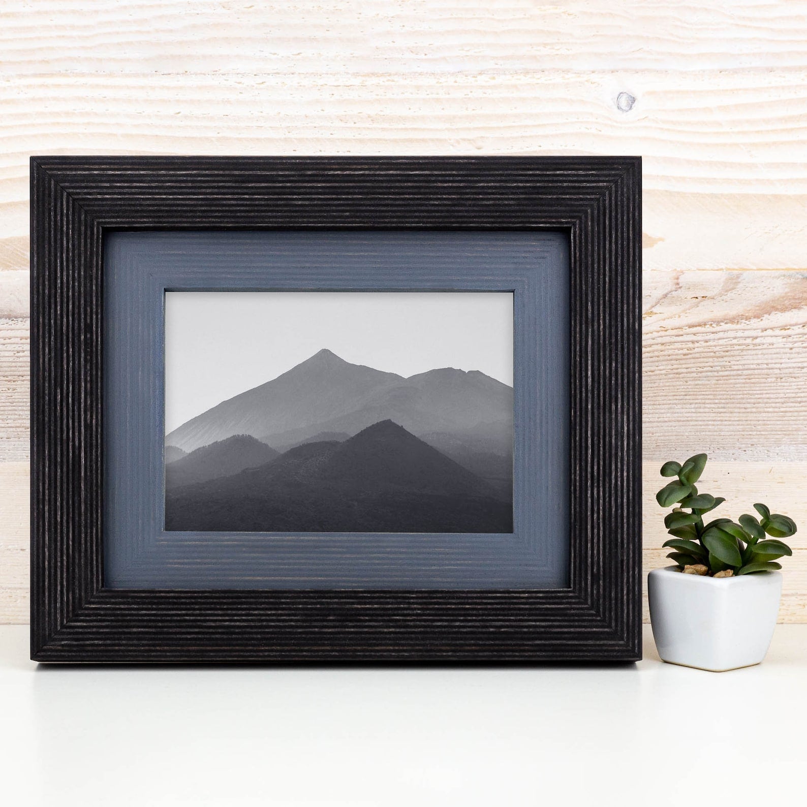 Framed black and white mountain landscape on a white surface with a plant in the background. Black + Grey Handmade Picture Frame, Photo Frame with Wooden Mat, Two Tone Poster Wall Frame, Custom Sizes A1 A2 5x7 8x10 18x24 24x36 20x30