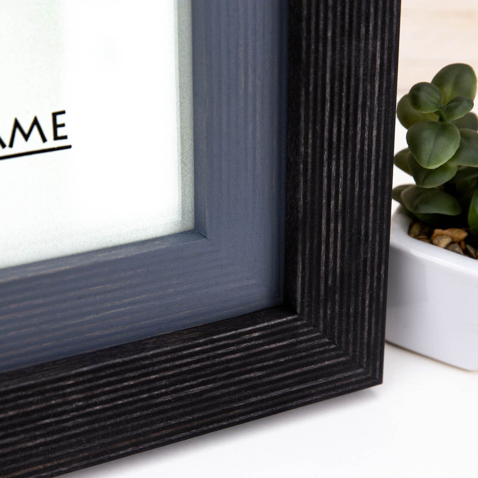 Close-up of a black picture frame with a plant in the background. Black + Grey Handmade Picture Frame, Photo Frame with Wooden Mat, Two Tone Poster Wall Frame, Custom Sizes A1 A2 5x7 8x10 18x24 24x36 20x30