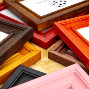 A collection of various solid birch hardwood picture frames in different colors including white, black, brown, red, and pink, with visible wood grain patterns.