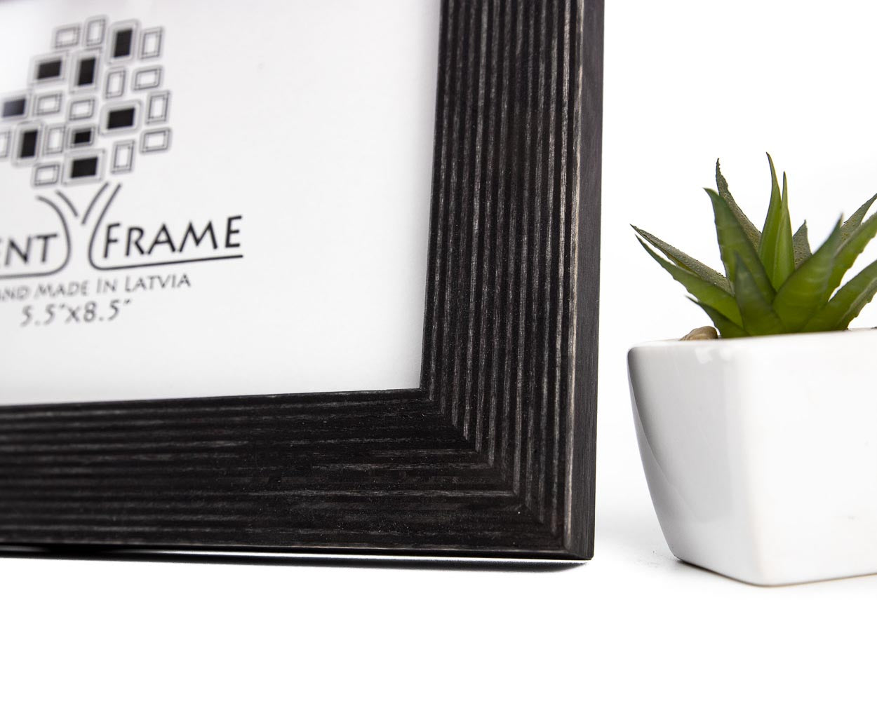 A black solid birch hardwood picture frame with a unique stripy design, displayed with a small potted plant to the side.