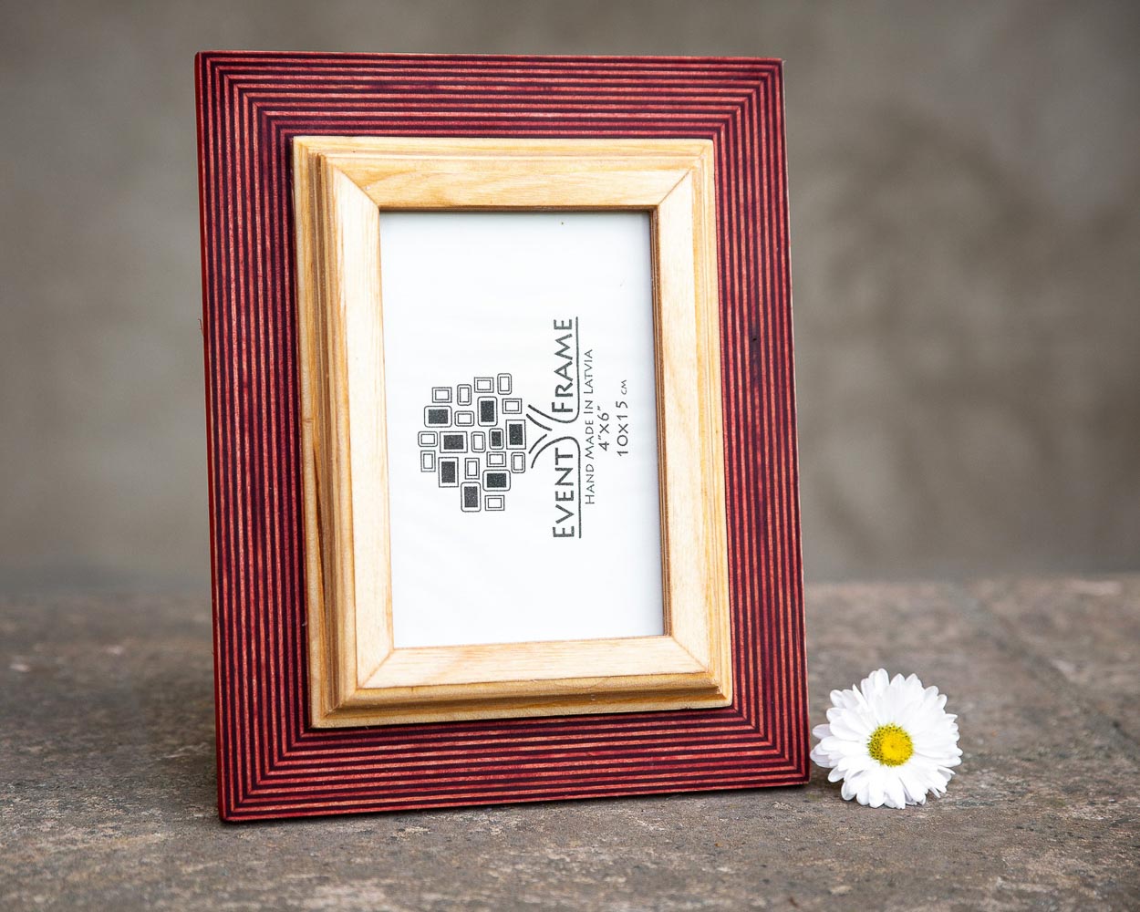 A rustic design picture frame with a red exterior and natural wood interior, displayed with a white artwork piece and a small flower beside it.