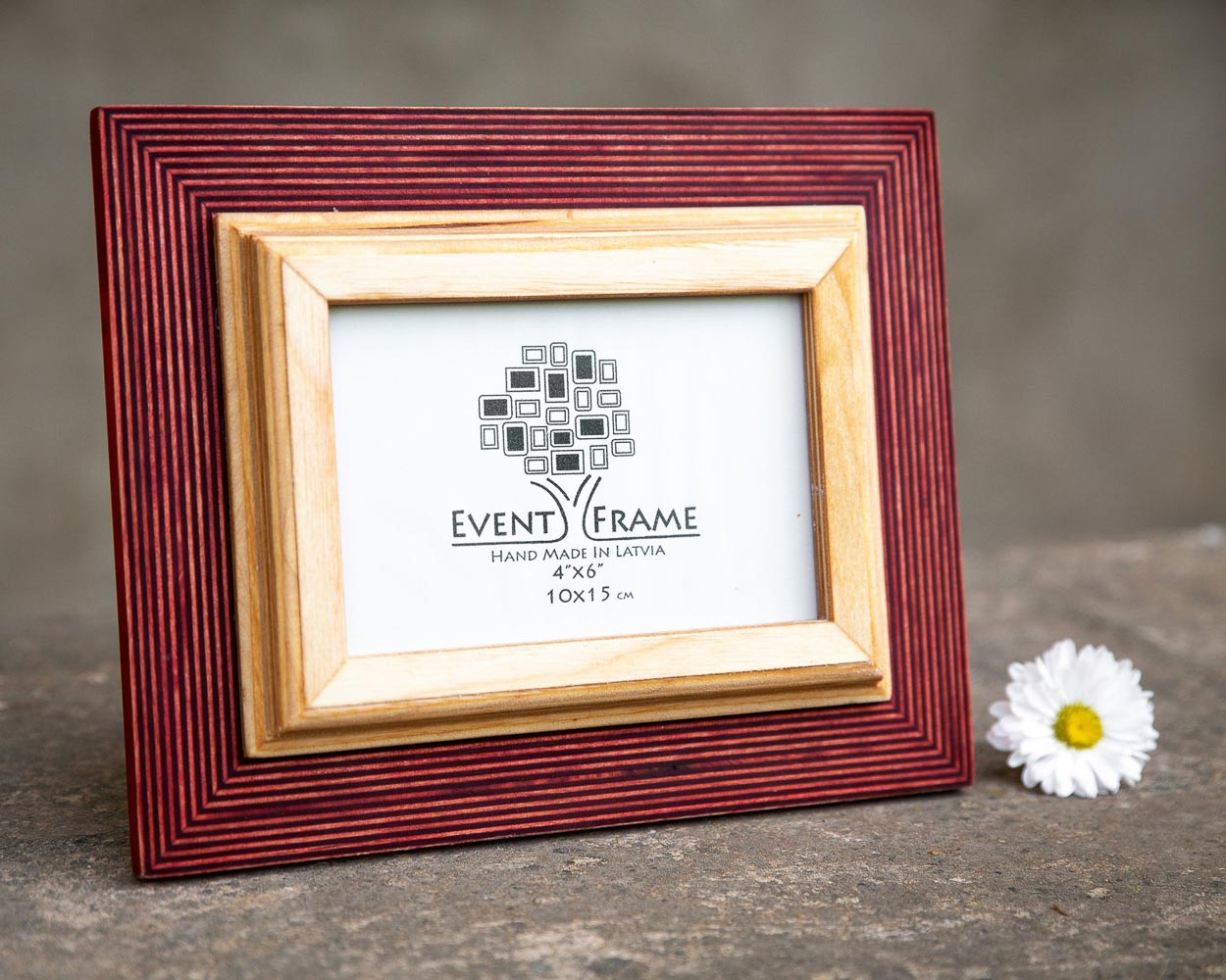 A rustic design picture frame with a red exterior and natural wood interior, displayed with a white artwork piece and a small flower beside it.