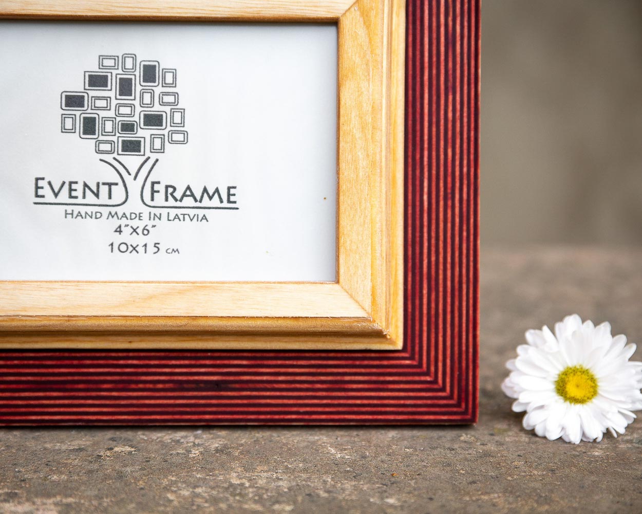 A rustic design picture frame with a red exterior and natural wood interior, displayed with a white artwork piece and a small flower beside it.