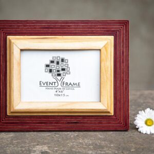 A rustic design picture frame with a red exterior and natural wood interior, displayed with a white artwork piece and a small flower beside it.